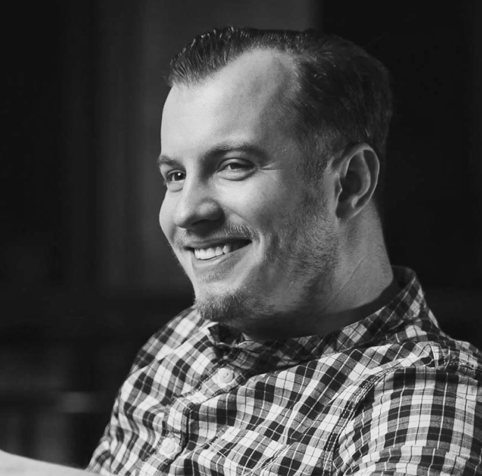 Portrait of a man with brown hair and glasses on a flat gray background.